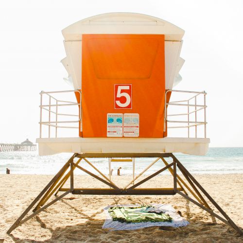 An orange lifeguard tower with a "5" sign on a sandy beach, with a pier in the background and a couple of towels spread out below it ends the sentence.